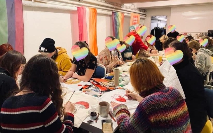 Grupa osób malujących w kreatywnej atmosferze, z tęczowymi flagami.