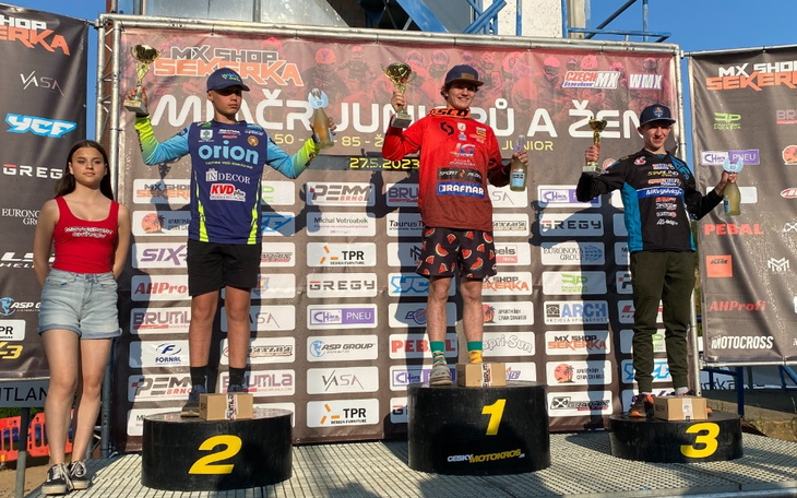 Zawodnicy na podium z pucharami, w tle baner z nazwą wydarzenia.