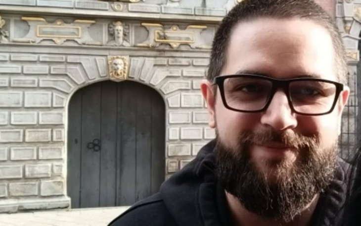 Mężczyzna z brodą i okularami, uśmiecha się do kamery.