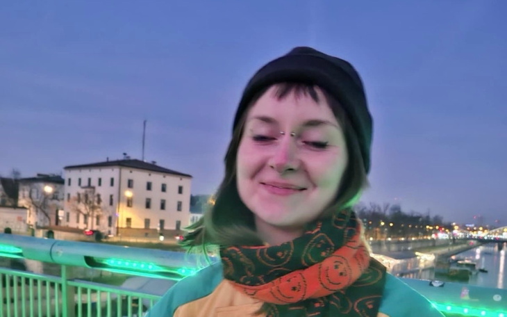 Uśmiechnięta dziewczyna na moście, w tle oświetlone miasto.