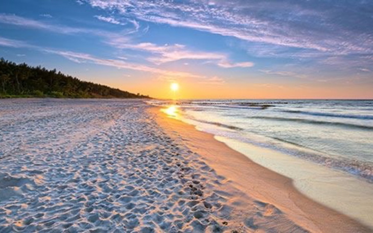 Plaża o zachodzie słońca, z falami i piaskiem.