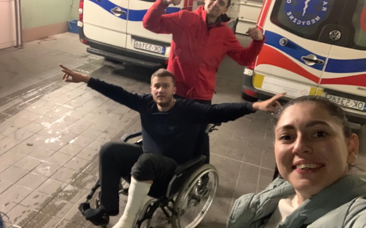 Trzy osoby pozujące w garażu, jedna na wózku inwalidzkim.