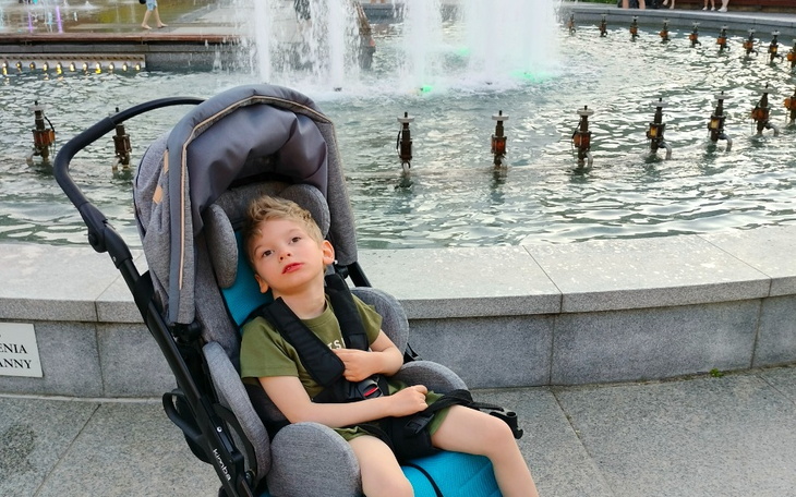 Chłopiec w wózku, siedzący przy fontannie.