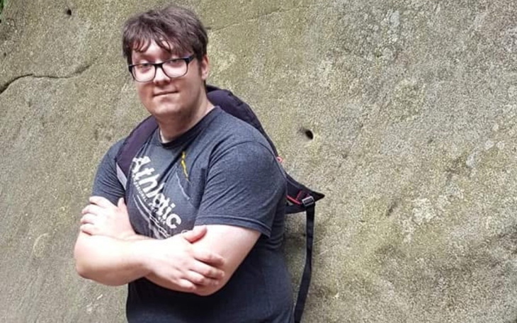 Młody mężczyzna pozujący na tle skały, z plecakiem na ramieniu.