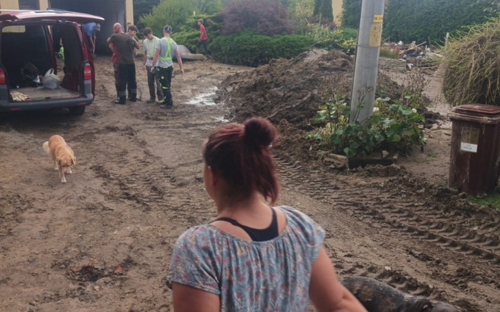 Wolontariusze pomagają w sprzątaniu po powodzi, w tle zniszczony teren.