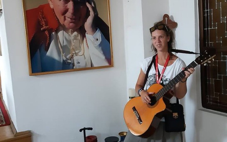 Kobieta grająca na gitarze, obok portret Jana Pawła II.