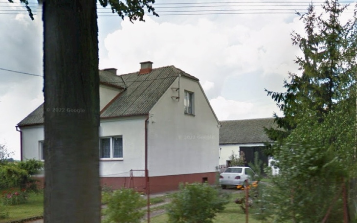 Dom na wsi z ogrodem i drzewami w tle.