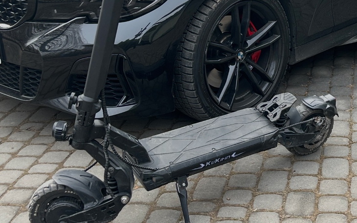 Skuter elektryczny obok czarnego samochodu na kostce brukowej.