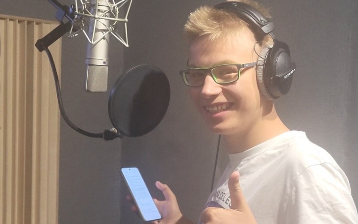 Młody mężczyzna w studiu nagraniowym, uśmiechnięty i trzymający telefon.