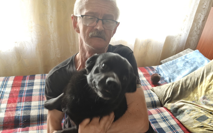 Mężczyzna trzyma czarnego psa na kanapie w domowym otoczeniu.