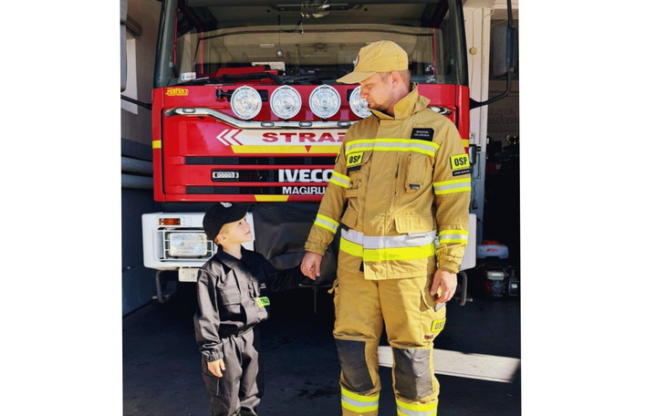 Strażak w pełnym umundurowaniu z dzieckiem, symbol odwagi i wsparcia.