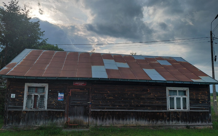 Stara, drewniana chata z uszkodzoną dachówką, w tle burzowe niebo.