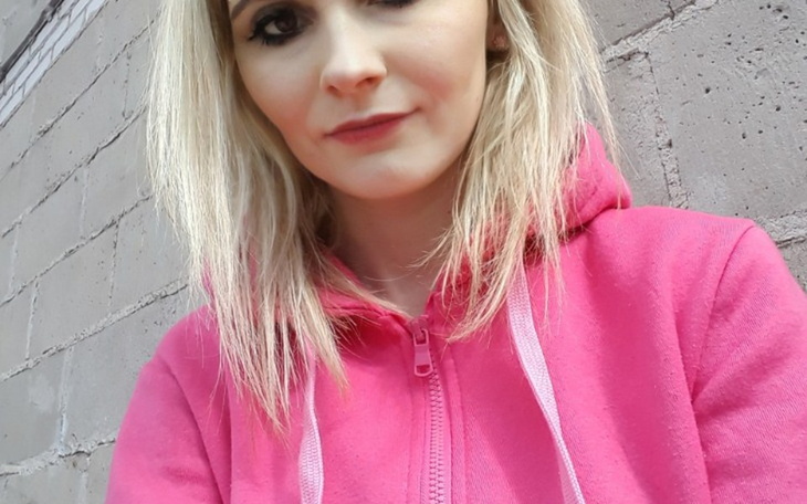 Kobieta w różowej bluzie, uśmiechająca się do kamery.