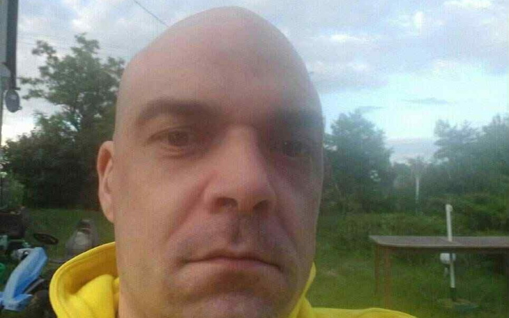 Mężczyzna z wyrazem twarzy pełnym powagi, na tle natury.
