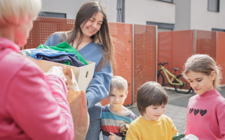 Młoda kobieta przekazująca ubrania dzieciom.