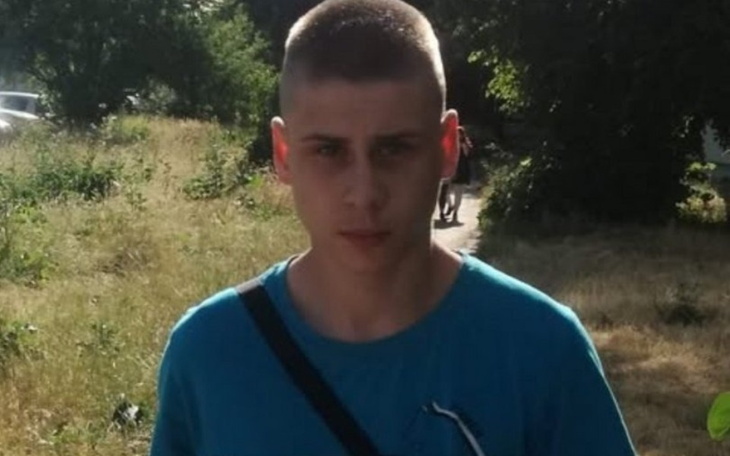 Młody mężczyzna w niebieskiej koszulce stoi na tle zieleni.