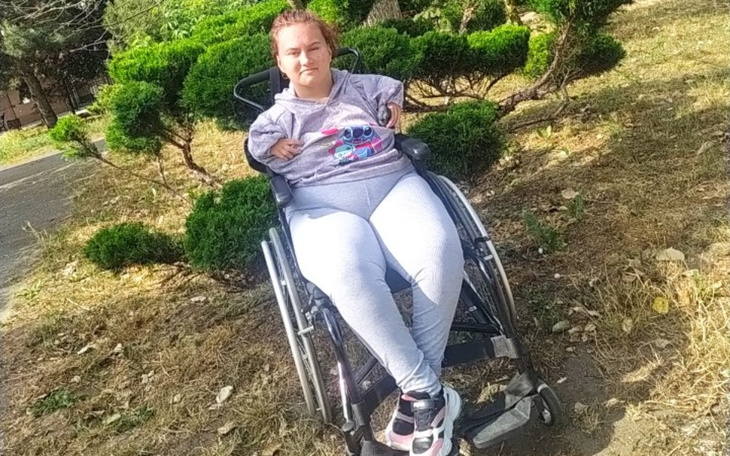 Dziewczyna na wózku inwalidzkim w parku, otoczona zielenią.