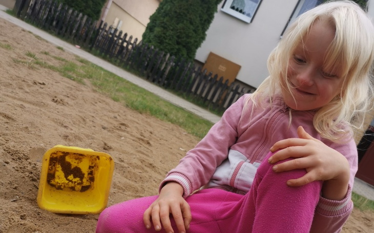 Dziecko bawiące się w piaskownicy, uśmiechnięte.