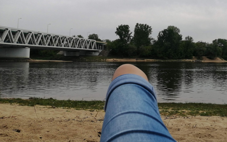 Widok na rzekę z plaży, z mostem w tle.