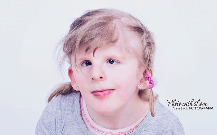 Portret dziewczynki z uśmiechem i różowymi kolczykami.