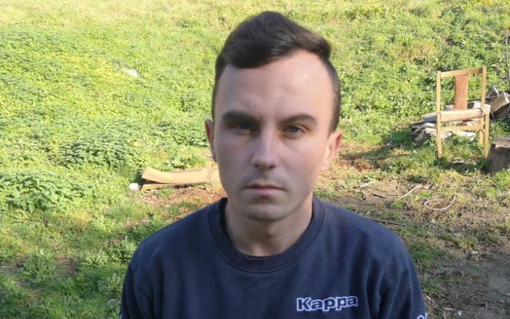 Mężczyzna na tle zielonej trawy, z poważnym wyrazem twarzy.