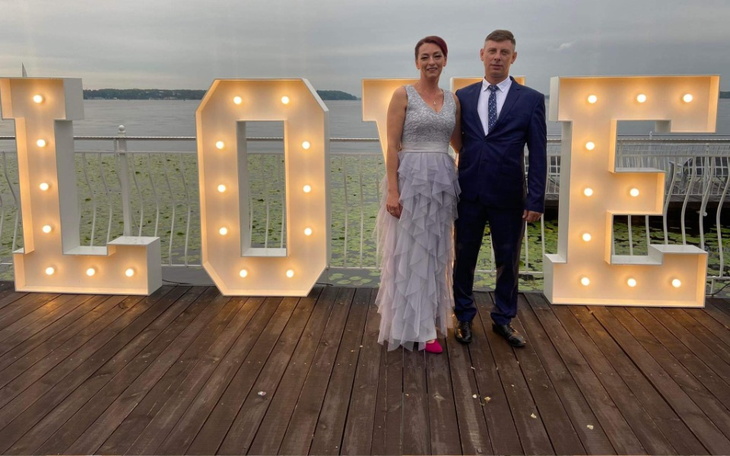 Para w eleganckich strojach, pozująca przy dużych literach 'LOVE'.