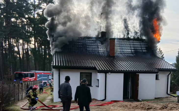 Dom w płomieniach, strażacy walczą z pożarem.