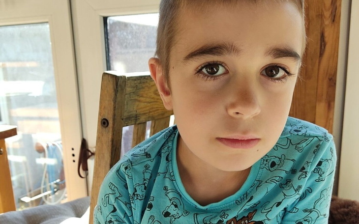 Chłopiec w niebieskiej koszulce, siedzący na krześle.