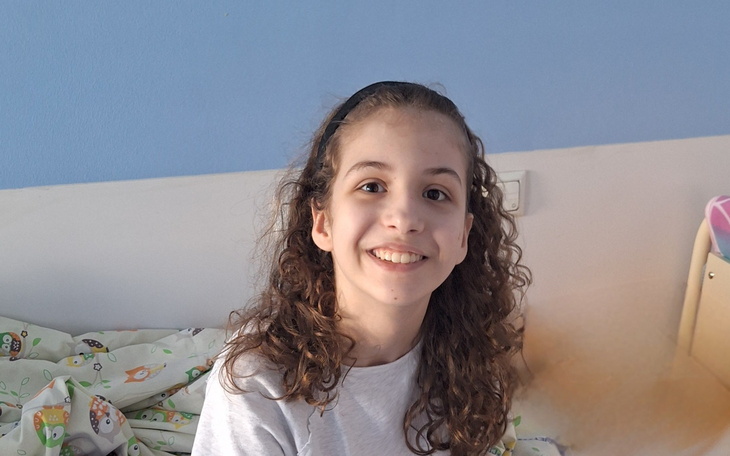 Uśmiechnięta dziewczynka siedząca na łóżku w pokoju.