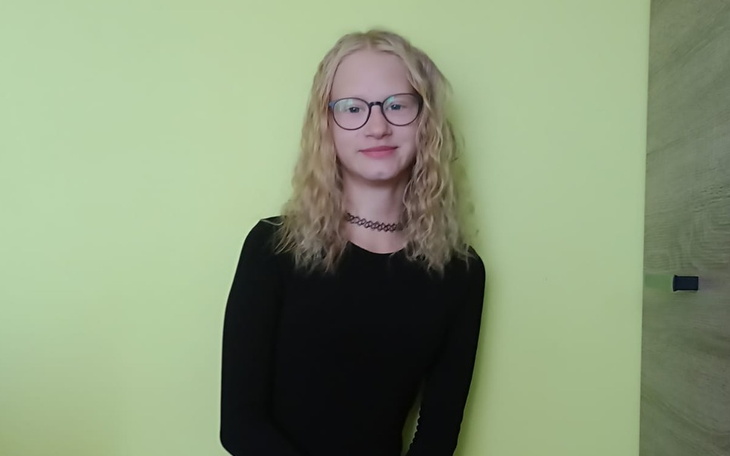 Młoda dziewczyna w czarnej bluzce na tle zielonej ściany.