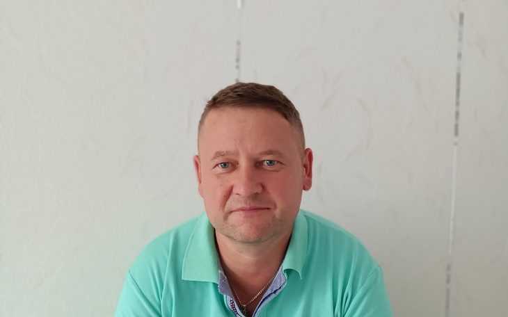 Blisko twarzy jubilera z butelką na tle białej ściany.
