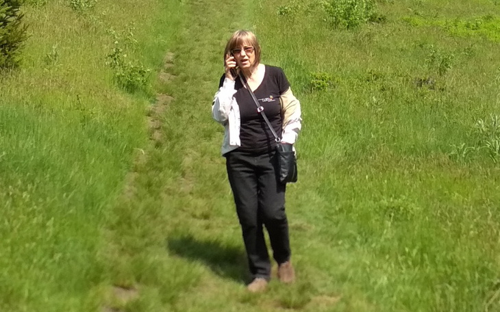 Kobieta spacerująca po zielonej łące, rozmawiająca przez telefon.