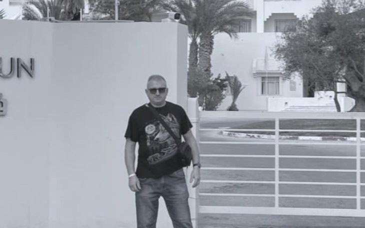 Mężczyzna w okularach przeciwsłonecznych, pozujący na tle budynku.