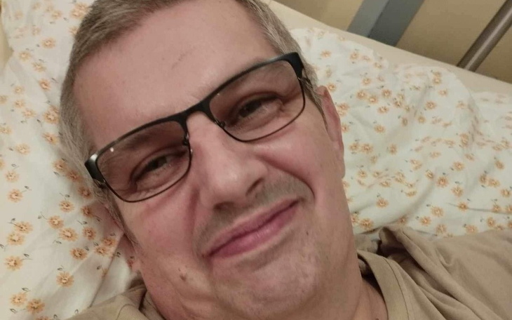Mężczyzna uśmiechający się w szpitalnym łóżku, w okularach.