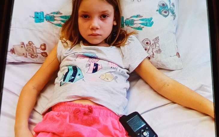 Chora dziewczynka leżąca w łóżku z telefonem.