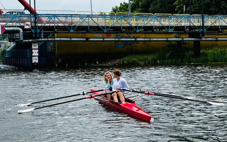 Dwie osoby w łódce wiosłowej na wodzie, w tle most.