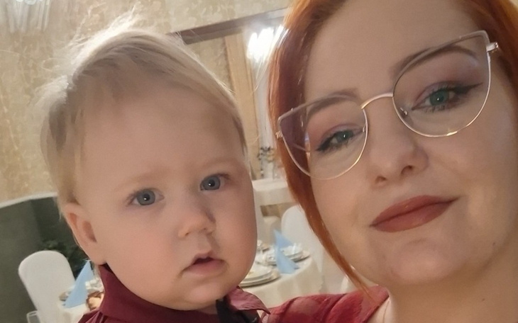 Kobieta z dzieckiem na rękach, oboje uśmiechnięci na przyjęciu.