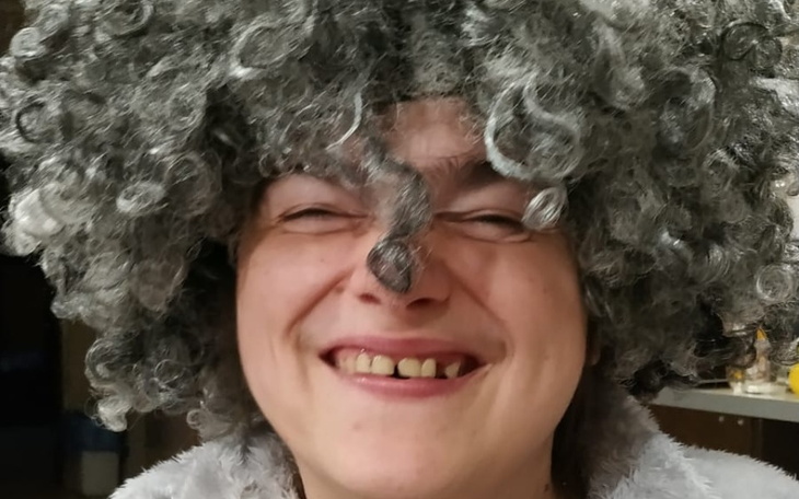 Osoba z kręconymi włosami w uśmiechu, w zabawnej stylizacji.