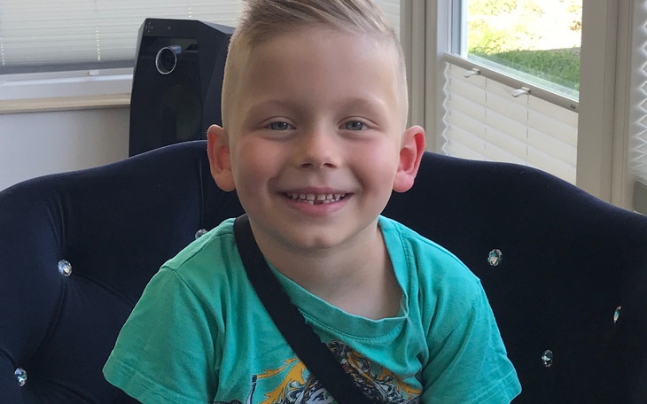 Uśmiechnięty chłopiec siedzący na kanapie, w zielonej koszulce.