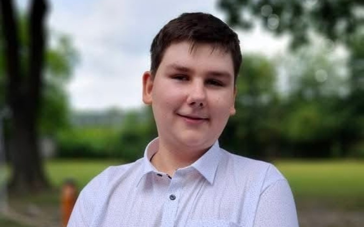 Młody chłopak uśmiechający się na tle zieleni.