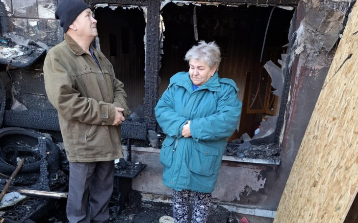 Mały pies w kolorowej kurtce, siedzący na miękkim kocu.