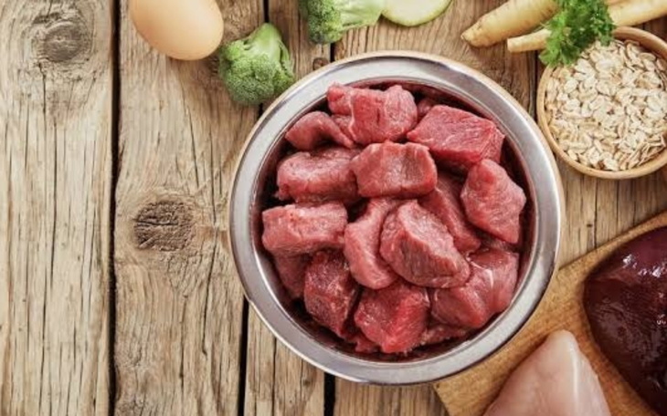 Surowe mięso w misce, otoczone warzywami i składnikami.