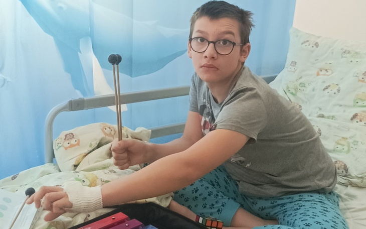 Chłopiec w łóżku, trzymający pałeczki do gry na instrumentach.