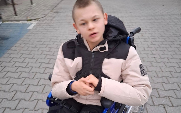 Chłopiec w wózku inwalidzkim, z zamyśloną miną na ulicy.