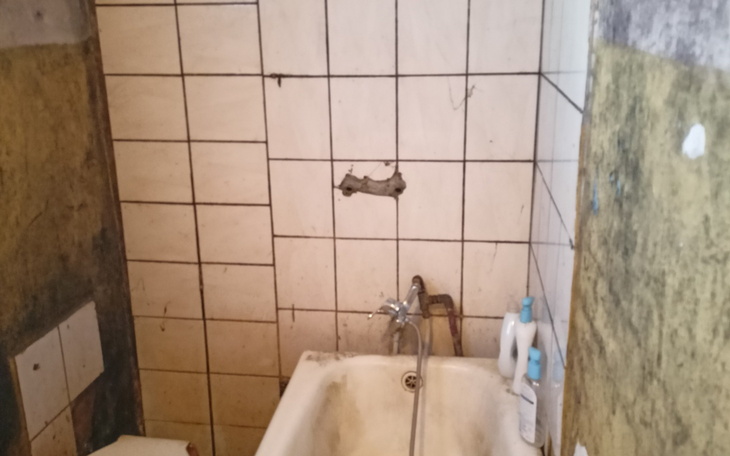 Zniszczona łazienka z brudnymi kafelkami i wanną.