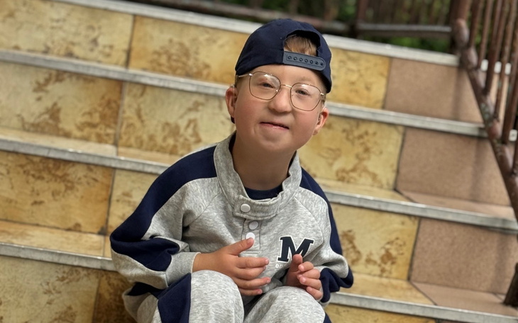 Chłopiec w szarej dresowej odzieży, uśmiechający się na schodach.