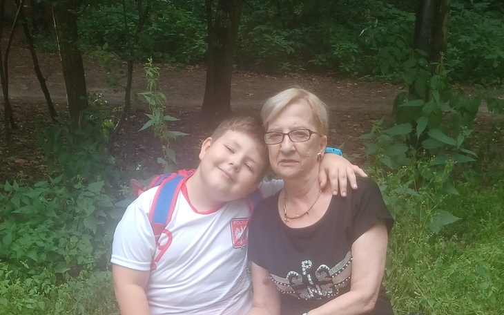 Chłopiec z babcią w lesie, uśmiechnięci i szczęśliwi.