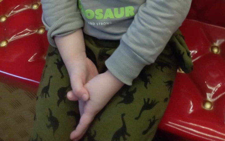 Dziecko z założonymi rękami, siedzące na czerwonej kanapie.