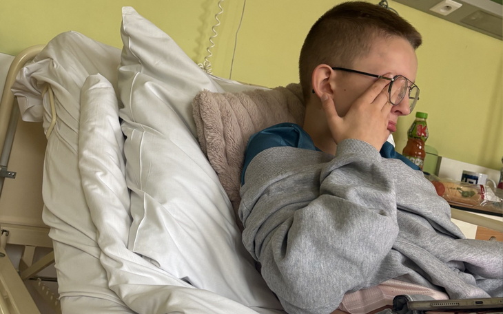 Chłopiec w szpitalnym łóżku, z wyrazem zmęczenia na twarzy.