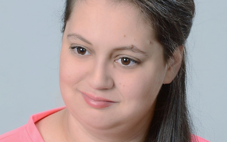 Portret młodej kobiety z delikatnym uśmiechem, w różowej bluzce.